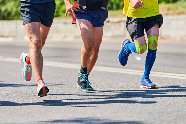 Juoksevia miehiä. Urheilijat lenkkeilevät urheiluvaatteissa kaupungin tiellä. Terveellinen elämäntapa, kunto harrastus. Street maraton kilpailu, sprinting ulkona - Valokuva, kuva