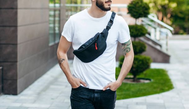Elegante hipster barbuto in città in una t-shirt bianca con marsupio - Foto, immagini