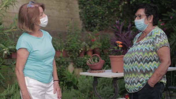 Twee volwassen vrouwen dragen beschermende gezichtsmaskers chatten - Video