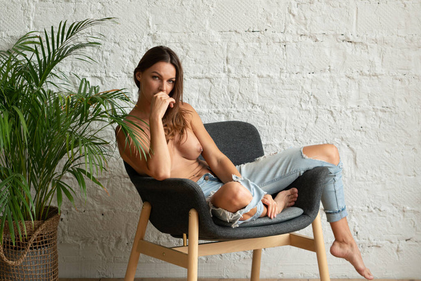молода красива дівчина позує оголеною в студії, сидячи на кріслі
 - Фото, зображення