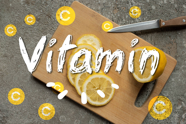 top view of sliced lemon on wooden cutting board with knife on grey concrete surface, vitamin illustration - Фото, изображение