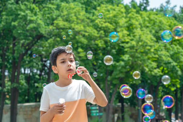 Πορτρέτο ενός νεαρού αγοριού φυσάει φυσαλίδες στο πάρκο για διακοπές - Φωτογραφία, εικόνα