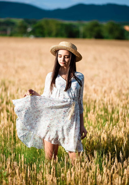 Retrato de una niña en un campo de trigo. Retrato de una hermosa niña con un vestido blanco y sombrero en un campo de trigo. Chica con un vestido blanco y sombrero. Campo de trigo. Retrato de una joven en la naturaleza
. - Foto, imagen