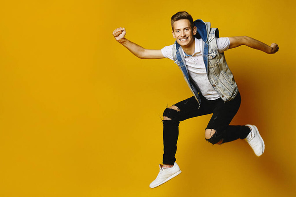 Side view of happy young hipster guy in denim clothes jumping at the yellow background, isolated. Advertising mockup with copy space - Foto, Imagem