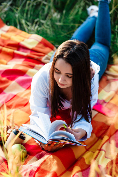 Retrato de uma rapariga num campo de trigo. A menina está deitada em um cobertor e lendo livros. Retrato de uma menina bonita em uma camisa em um campo de trigo. Campo de trigo
. - Foto, Imagem