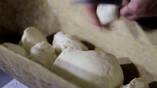 Een vrouw snijdt het deeg in stukken met een mes in een houten kneedbak - Video