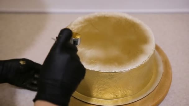 Snoepgoed bedekt een taart van een spuitpistool glazuur met gouden glanzende coating. Bakkers handen versieren de taart - Video