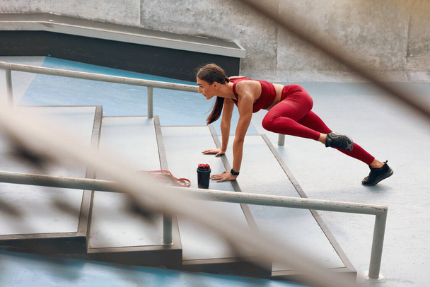 Woman Warming Up On Stairs Before Fitness Workout. Fit Girl In Fashion Sporty Outfit Exercising On Stadium. Female With Athletic Muscular Body Training Outdoor. Training In City As Urban Lifestyle. - Фото, изображение