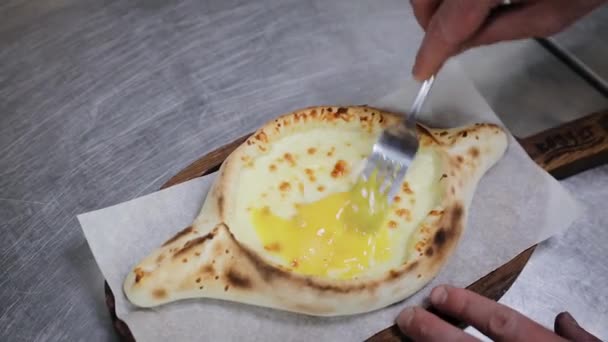 Ingredienti mescolanti a mano di khachapuri aiutante con forchetta in ristorante. Torta di pane aperta con formaggio e tuorlo d'uovo. Deliziosa cucina georgiana. - Filmati, video