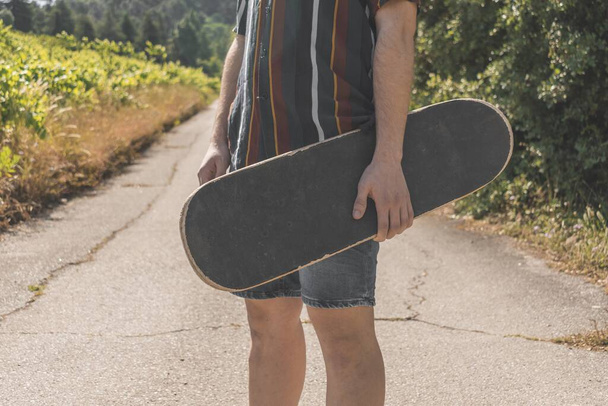 A closeup of a person holding a skateboard in a field under the sunlight - Foto, immagini