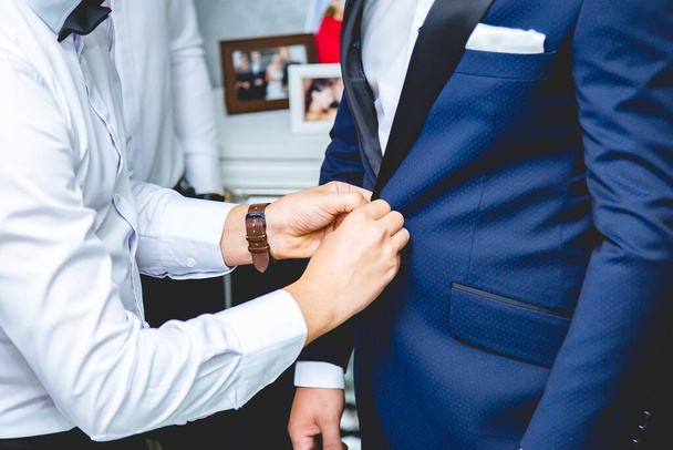 A closeup shot of groomsman helps the groom buttoning his suit - 写真・画像