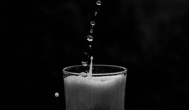 A closeup shot of a glass of refreshing soda drink with splashes on a black background - Foto, imagen