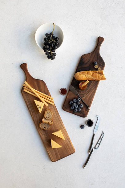 A vertical high angle shot of chopping boards with bread, cheese and berries on a white surface with aesthetic decoration - Foto, Imagem