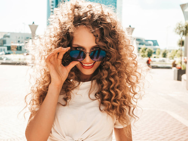 Portrait of beautiful smiling model with afro curls hairstyle dressed in summer hipster clothes.Sexy carefree girl posing in the street background. Trendy funny and positive woman having fun - Foto, Imagem