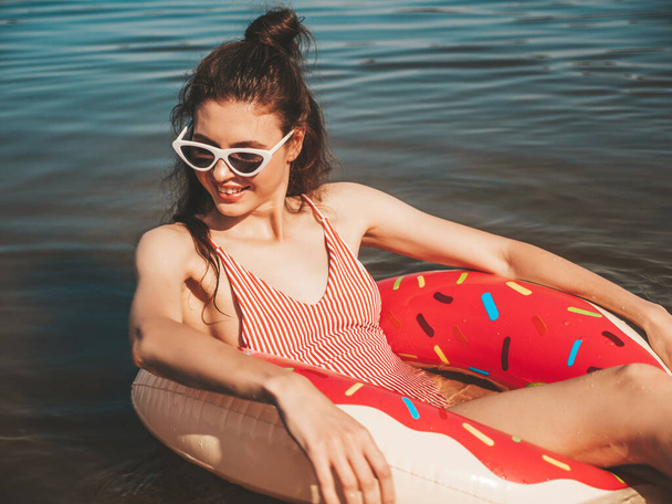 Young beautiful sexy smiling hipster woman in sunglasses.Girl in summer swimwear bathing suit swimming and lying in donut lilo inflatable mattress.Positive female relaxing in lake water - Фото, зображення