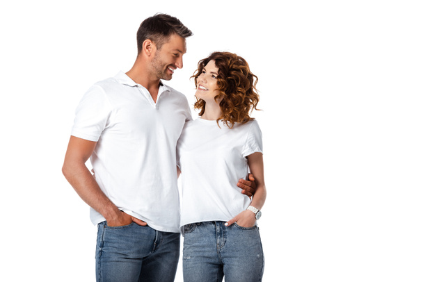 Mutlu bir adam ve kadın, elleri ceplerinde birbirlerine bakarken beyazlar içinde izole bir şekilde duruyorlar.  - Fotoğraf, Görsel
