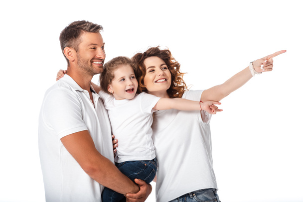 happy mother pointing with finger near cheerful husband holding in arms kid isolated on white  - Photo, Image