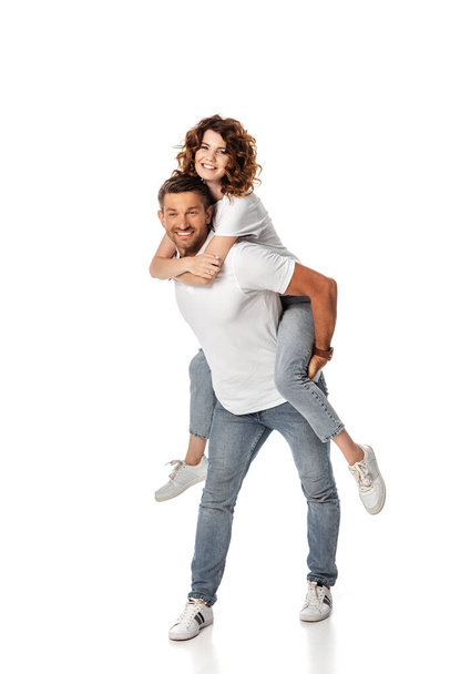 cheerful man piggybacking curly and happy wife on white  - Foto, afbeelding