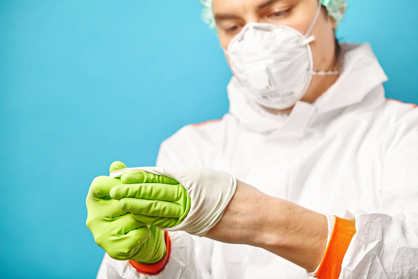 Doctor after medical procedure removes a sterile glove, close-up frame on blue background. - 写真・画像