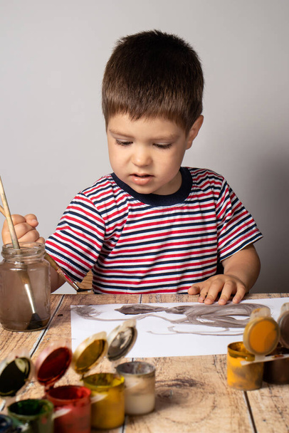 Маленький мальчик 2-3 года в полосатой яркой футболке рисует картину цветов гуаши. Красочный рисунок, детское творчество
. - Фото, изображение