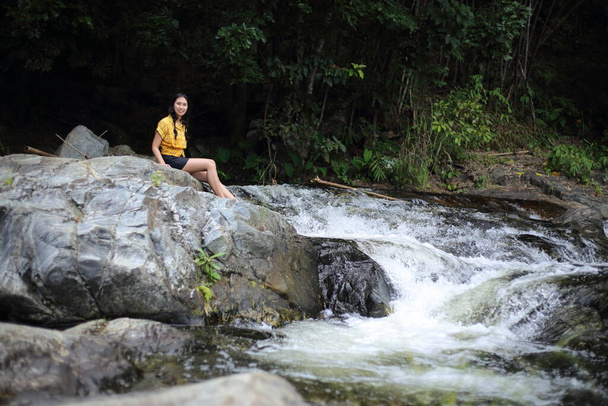 Žena sedící u vodopádu Khlong Nam Lai v národním parku Klong Lan, Kamphaeng Phet, Thajsko - Fotografie, Obrázek