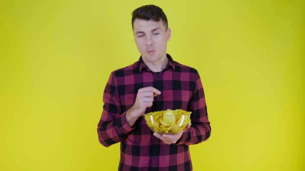 Uomo in camicia a quadri rosa mangia patatine fritte con ciotola di vetro su sfondo giallo - Filmati, video