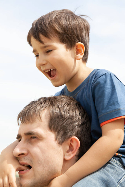 Концепция семьи и счастливого образа жизни. Мальчик сидит на шее своего отца
. - Фото, изображение