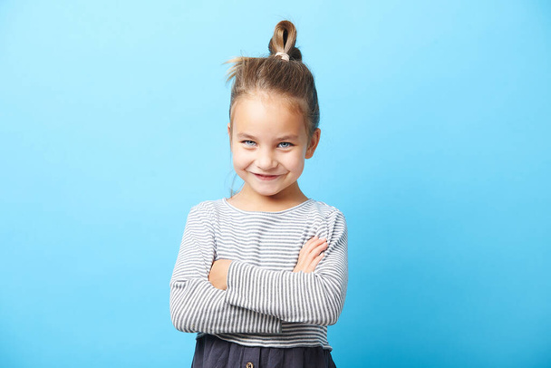Beautiful little girl smiling, crossed her hands, has a positive expression, standing on blue isolated. - Fotoğraf, Görsel