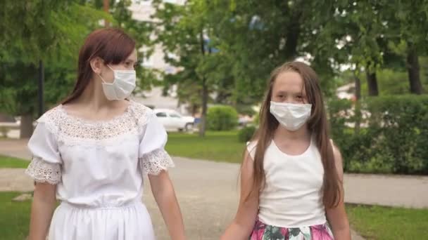 two girls in protective masks on their faces outdoors in a park. girls on a city street travel in a medical mask. tourists virus protection. go masked outdoors against bacteria - 映像、動画