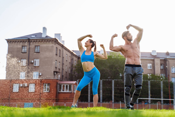 Exercises in pairs. Attractive athletes girl and guy demonstrating pumped up body. Long shot of bodybuilders posing at the stadium. Showing muscles on the arms. - Zdjęcie, obraz