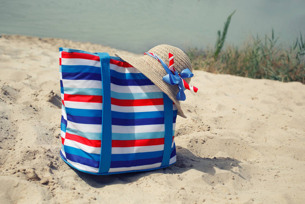 Accesorios de mujer de moda de playa con bolsa de rayas de lona y sombrero de paja con cintas en el río, fondo de la costa marina
 - Foto, imagen
