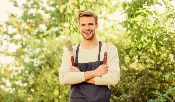 Barbecue utensils. Cooking burgers. Man hold barbeque equipment. Picnic concept. Bbq chef. Summer weekend. Tools for roasting meat outdoors. Barbeque party. Handsome guy cooking food. Grilling food - 写真・画像