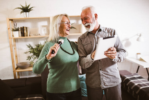 Senior couple singing karaoke at home, having fun. - Photo, Image