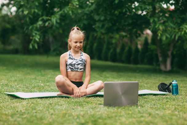 Uma adolescente pratica uma aula on-line ao ar livre perto de sua casa durante o auto-isolamento de quarentena durante uma pandemia. A praticar desporto. Estilo de vida saudável
 - Foto, Imagem