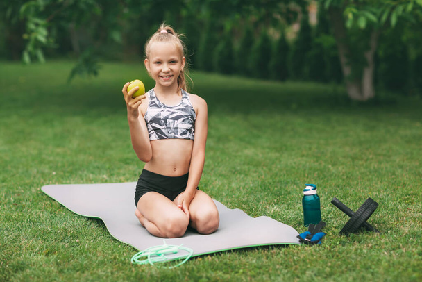 Ein Mädchen im Teenageralter hält einen Apfel und eine Banane in der Hand, nachdem sie in der Nähe ihres Hauses ein Online-Outdoor-Training absolviert hat. Sport. Gesunder Lebensstil - Foto, Bild