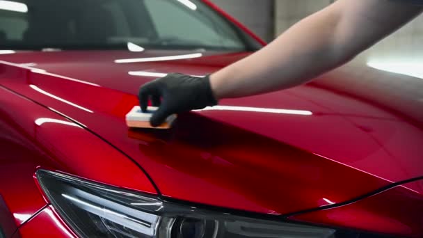 Dettagli dell'auto: l'uomo applica un rivestimento nano protettivo o cera sull'auto rossa. Coprire il cofano dell'auto con uno smalto di vetro liquido. - Filmati, video