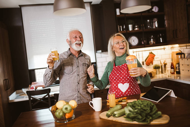 Beau couple de personnes âgées danse et sourit tout en cuisinant ensemble dans la cuisine - Photo, image