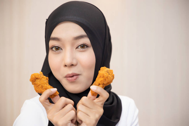 éhes iszlám nő keres, eszik halal sült csirke szárnyasbot; fogalma finom halal élelmiszer, gyorsétterem, egészségügyi ellátás, étkezési szokások, ropogós ízletes sült csirke burger; ázsiai muszlim nő modell - Fotó, kép