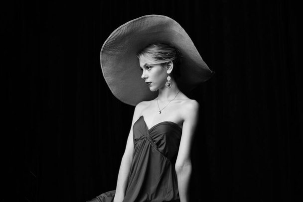 Geniş kenarlı şapkalı, bordo bir gece elbisesiyle siyah arka planda poz veren güzel bir kız. - Fotoğraf, Görsel