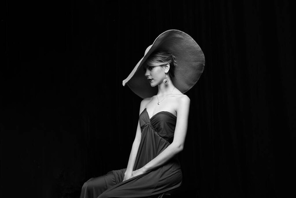 gyönyörű lány széles karimájú kalap és egy burgundi estélyi ruha pózol a fekete háttér - Fotó, kép