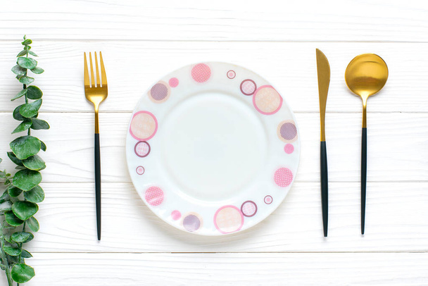 plato redondo blanco vacío, tenedor, cuchillo, cuchara, ramita de eucalipto sobre mesa de madera Vista superior Platos para el desayuno, el almuerzo o la cena
 - Foto, Imagen