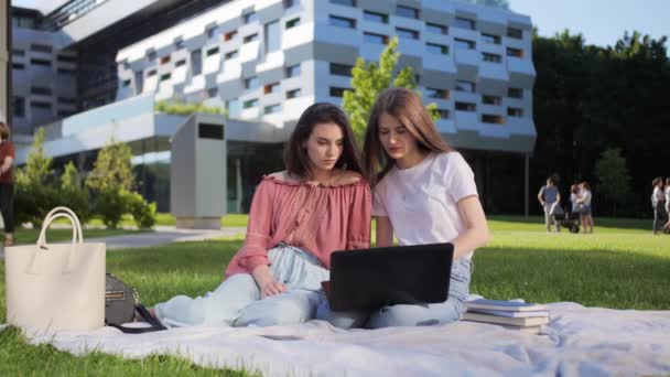 Zwei hübsche Studentinnen studieren auf einem Laptop im Freien vor dem Hintergrund der Universität eine Vorlesung. - Filmmaterial, Video