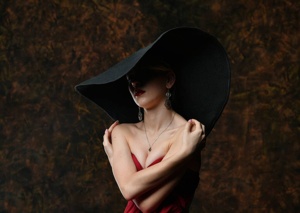 krásná dívka v černém klobouku a vínové večerní šaty zabalila se do náruče - Fotografie, Obrázek