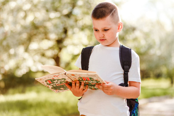 Junge im weißen T-Shirt mit einem Buch in der Hand im Sommer draußen - Foto, Bild