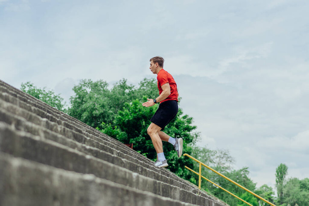 Подходящий спортсмен, выполняющий упражнения на лестницах, бегущий вверх по лестнице, выполняя упражнения на открытом воздухе. - Фото, изображение