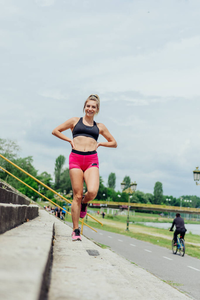 Apto atleta saudável, mulher bonita em sportswear apertado pulando em escadas, aquecendo-se antes de correr, enquanto parece altamente motivado. - Foto, Imagem