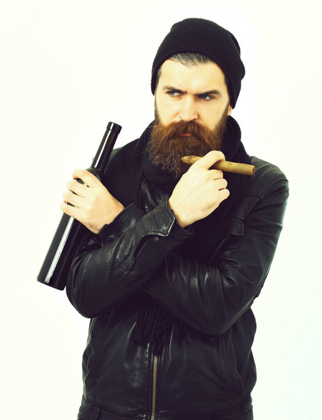 Bearded brutal caucasian hipster holding bottle and smoking cigar - 写真・画像