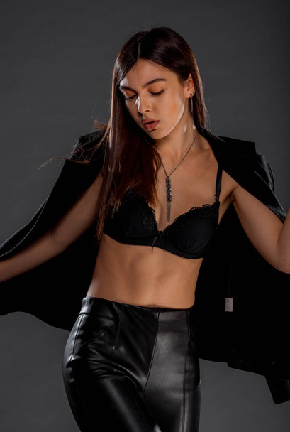 Πορτρέτο ενός όμορφου γυναικείου μοντέλου ποζάρει σε μοντέρνο μαύρο σουτιέν και δερμάτινο παντελόνι - Φωτογραφία, εικόνα
