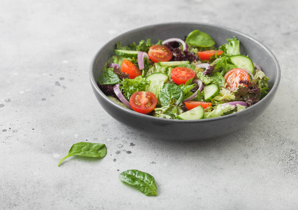 Healthy fresh vegetables salad with cucumbers and tomatoes, red onion and spinach in grey bowl on dark background with pepper - Foto, immagini