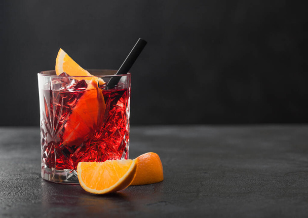 Negroni cocktail in crystal glass with orange slice and black straw on black table background. - Fotografie, Obrázek